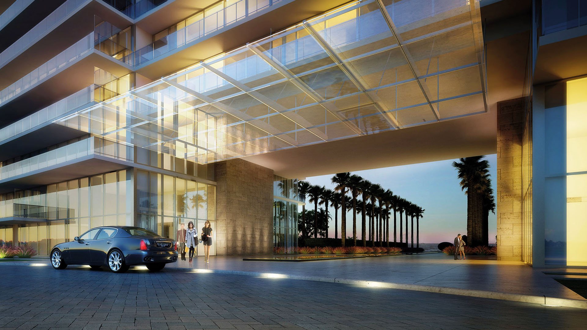 Dusk porte cochere at Oceana Key Biscayne in Key Biscayne, showcasing luxury and ultra luxury condos with a dramatic glass canopy, illuminated arrival court, palm-lined drive, and ocean beyond.