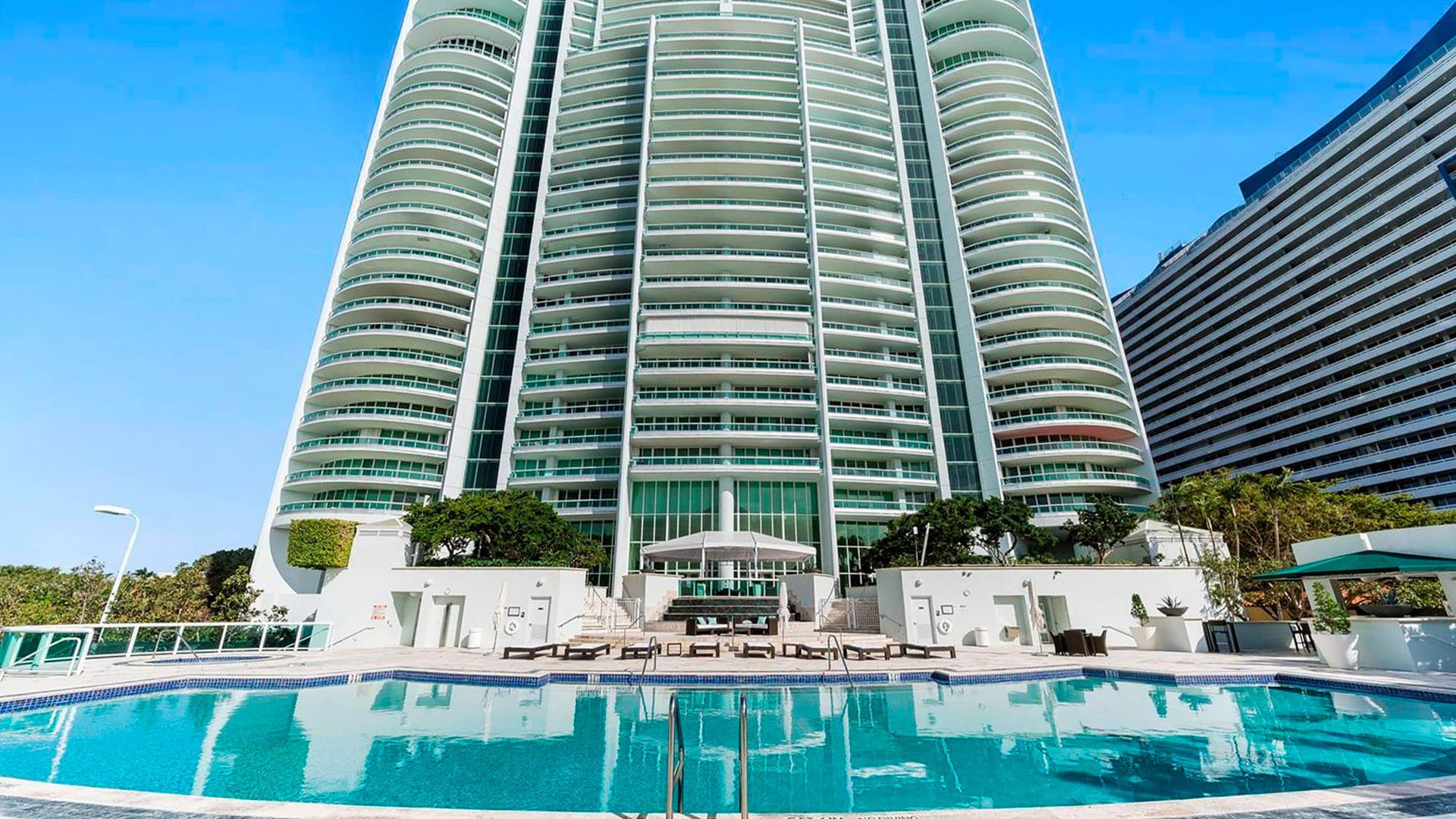 Resort-style pool and tower exterior at Santa Maria in Brickell, presenting luxury and ultra luxury condos with curved balcony lines, sun deck seating, and a dramatic high-rise facade.